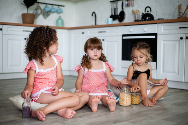 Kleine Mädchen werden in der Küche gespielt, während sie auf dem Fußboden sitzen. - Foto, Bild