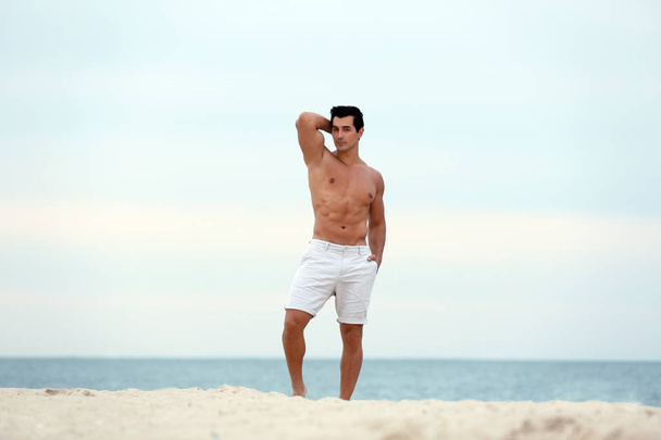Handsome young man posing on beach near sea - Zdjęcie, obraz