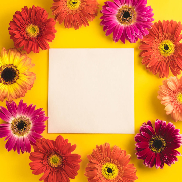 Bright beautiful gerbera flowers and paper card on a sunny yellow background. Mothers Day, Valentine holiday. Place for text, lettering or product. View from above, Copy space. Flatlay. - Foto, immagini