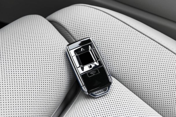 Closeup inside vehicle of wireless blue leather key ignition on white leather seat. Wireless start engine key. Car key remote isolated. Modern Car keys. Car keys close up. White perforated leather interior - 写真・画像