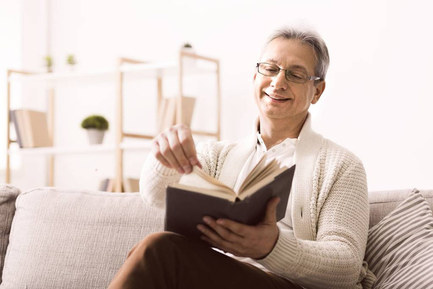 Hombre mayor en gafas disfrutando de un buen libro con sonrisa
 - Foto, Imagen