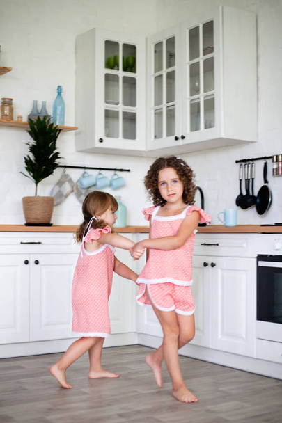 Дві маленькі дівчата носять нічні сукні. Розважаючись на кухні. Розмитий фокус
. - Фото, зображення