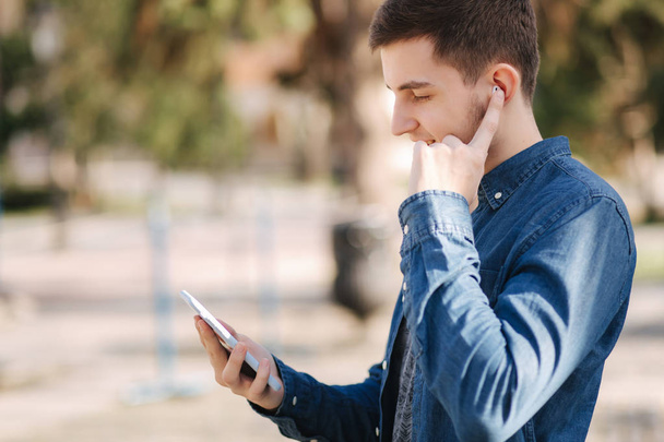 Jonge man gebruik van telefoon en draadloze hoofdtelefoon en print bericht in sociaal netwerk - Foto, afbeelding