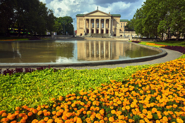 Macizos de flores, estanque y fachada del histórico edificio de ópera de Poznan
 - Foto, imagen