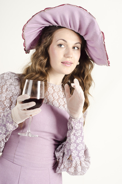 Studio portrait of beautiful woman dressed in old fashinable style and a wide hat with a glass of wine - Foto, immagini