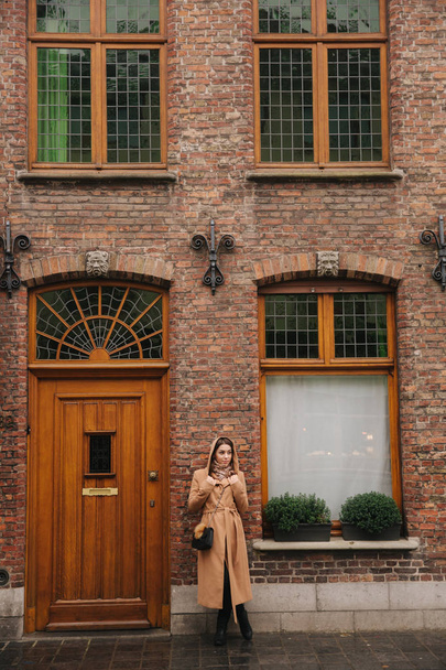Stylish woman in brown coat standing on the bridge in Bealgium, Brugge. Female put on a hood - Fotó, kép