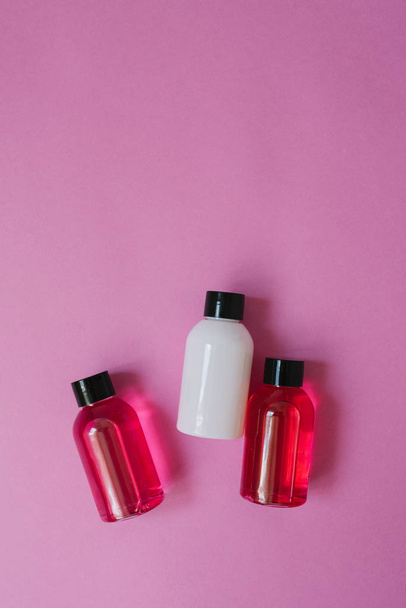 Groep van kleine reis flessen voor lichaamsverzorging: douchegel, shampoo, balsem, lotion op roze achtergrond. De samenstelling van de platte laag van cosmetica Kopieer ruimte. - Foto, afbeelding