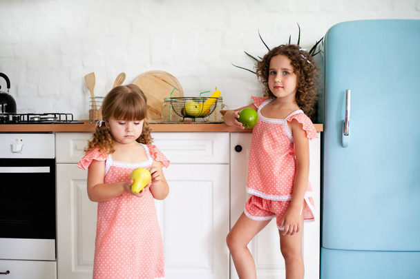 Due bambine in cucina con la frutta. Bambini vicino al frigorifero con cibo sano
. - Foto, immagini