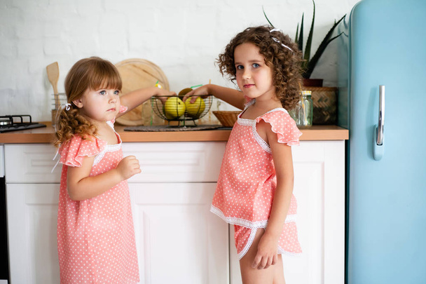 果物と台所で2人の小さな女の子。冷蔵庫の近くに良い食べ物を持つ子供たち. - 写真・画像