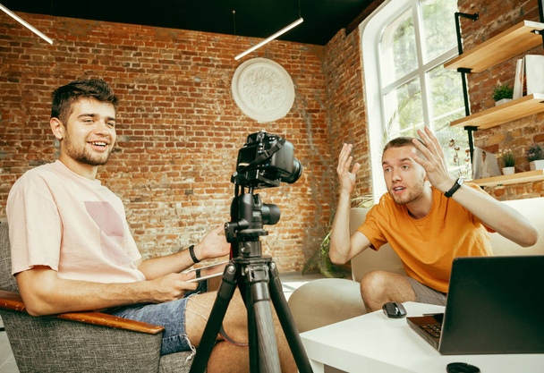 Two young male bloggers with professional camera recording video interview at home - Photo, Image