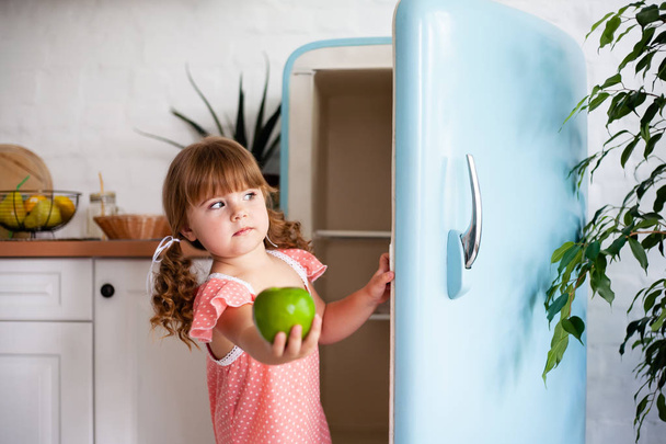 Küçük bir kız buzdolabının kapısını açar. Güzel mutfak. - Fotoğraf, Görsel