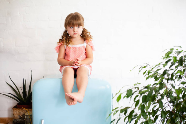 Pikkutyttö istuu jääkaapin päällä. Istuu kaunis retro jääkaappi sininen väri, tyylikäs sisustus
. - Valokuva, kuva