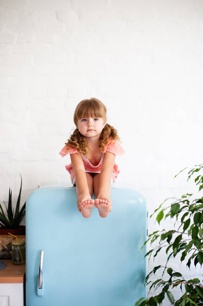 Kislány ül a hűtőszekrényben. Ül egy gyönyörű retro hűtő, kék színű, stílusos belső. - Fotó, kép