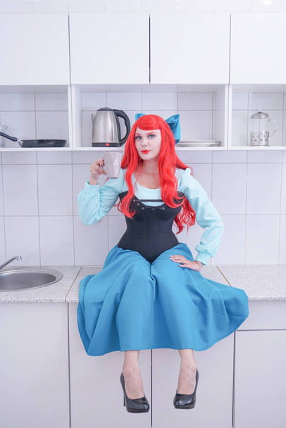 Jong rood haar meisje in blauwe jurk met zwart korset op de keuken - Foto, afbeelding