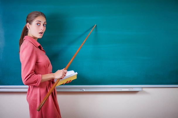Genç kadın öğretmen bir işaretçi ile bir tahta duruyor. Okul zaman çizelgesi ve diğer bilgiler için şablon. Güzel zımni okul panosunda boş kopya alanı gösterir. Eğitim kavramı. - Fotoğraf, Görsel