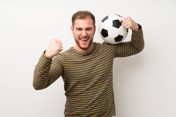Pohledný muž přes izolovanou bílou zeď držící fotbalový míč - Fotografie, Obrázek
