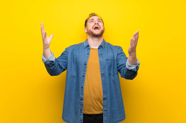 Blondi mies yli eristetty keltainen seinä huutaa eteen suu auki
 - Valokuva, kuva