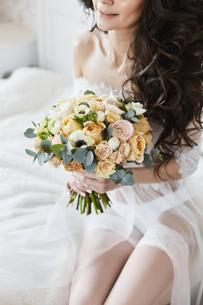 Tender bride with hairstyle sitting and keeping bouquet of fresh flowers - Fotografie, Obrázek
