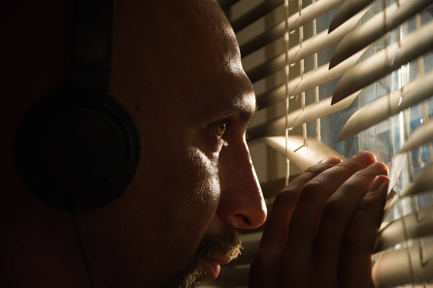 Agente secreto del FBI mira a través de las persianas y escucha la conversación en los auriculares
 - Foto, Imagen