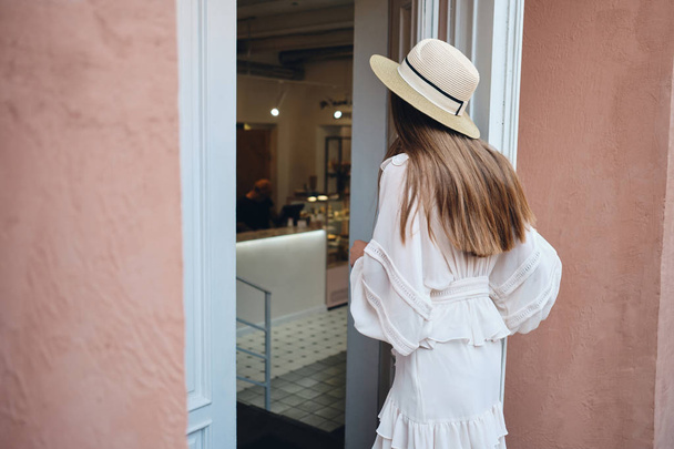 Jeune belle femme en robe blanche et chapeau de paille debout de l'arrière et l'ouverture de la porte blanche du café
 - Photo, image