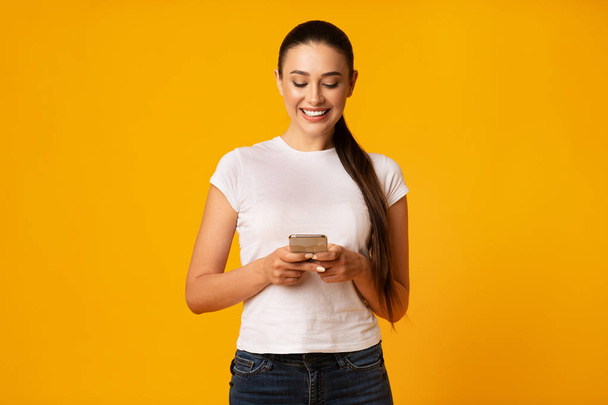 Iloinen tyttö chattailuun ystävien kanssa käyttäen matkapuhelin keltaisella taustalla
 - Valokuva, kuva