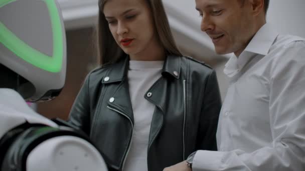 Um homem e uma mulher no shopping interagem com um consultor robô tocando na tela e sorrindo. Cyborg Android ajuda as pessoas
. - Filmagem, Vídeo