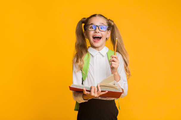 Heyecanlı İlköğretim Kız Öğrenci Tutan Kitap Ve Kalem Sarı Arka Plan - Fotoğraf, Görsel
