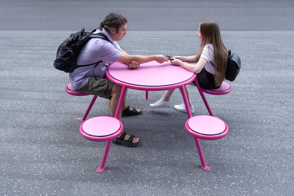 Genç bir adam ve kız sokakta pembe bir masada oturuyorlar.. - Fotoğraf, Görsel