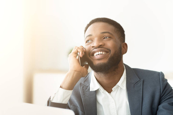 Счастливый молодой африканский мужчина говорит по телефону и выражает позитив
 - Фото, изображение