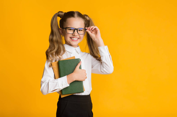 Mutlu okul kız sarı arka plan üzerinde kitap tutan, stüdyo çekim - Fotoğraf, Görsel