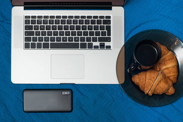 Typical blogger morning. Laptop and smartphone on the bed. Croissants with tasty coffee - Foto, immagini
