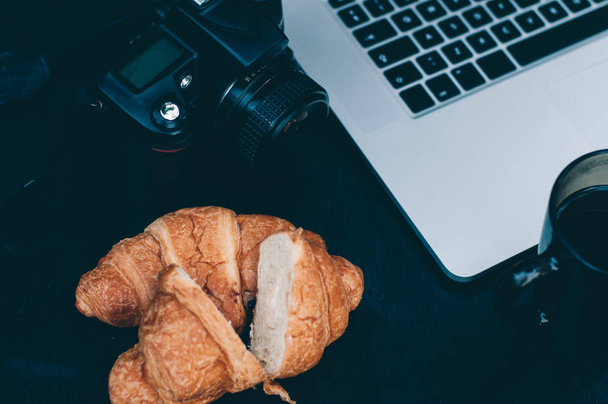 Typical photographer / blogger workplace in the morning. DSLR camera and laptop. Tasty croissants and cup of hot coffee - Фото, зображення