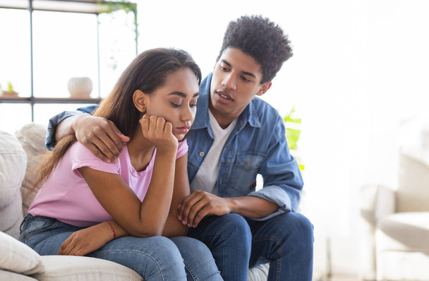 Young african guy comforting his sad girlfriend sitting on sofa - Photo, Image