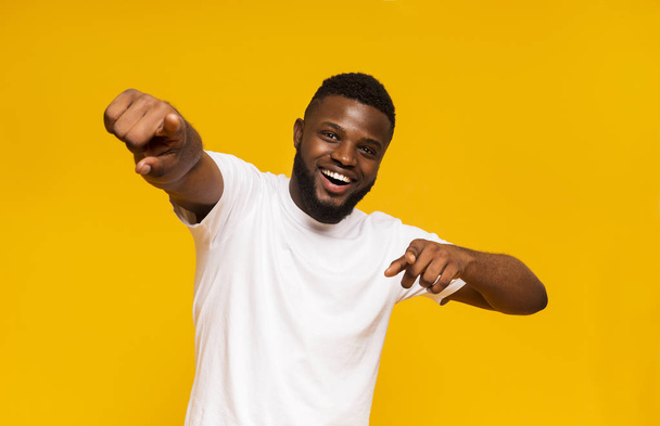 Homem africano alegre alegremente indicando na câmera, fundo de estúdio amarelo
 - Foto, Imagem