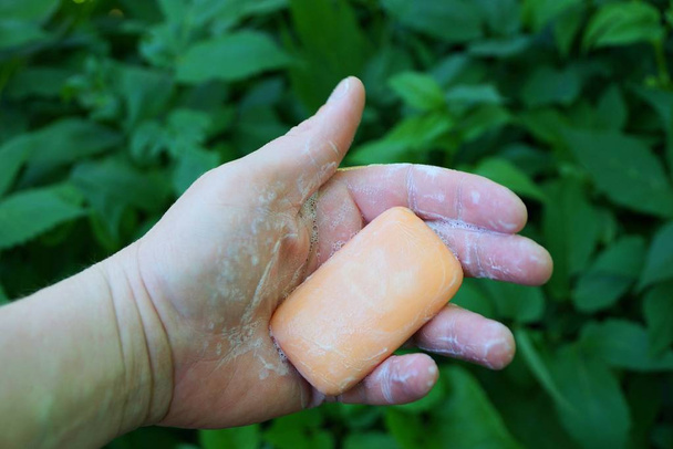 Vaaleanpunainen saippua vaahdotettu käsi taustalla vihreä kasvillisuus
 - Valokuva, kuva