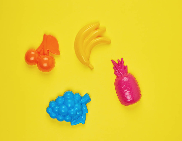 multicolored plastic toys fruits on a yellow  background - 写真・画像