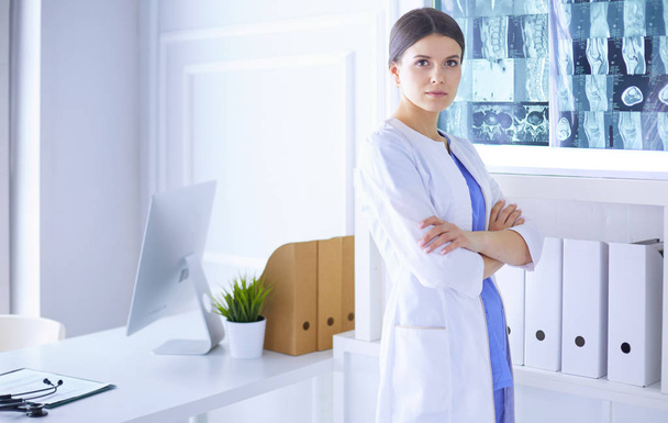 Portrait of young female doctor in white coat standing in hospital with her hands crossed - Photo, Image