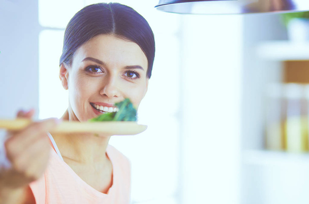 Mosolygó fiatal nő keverés friss saláta a konyhában. - Fotó, kép