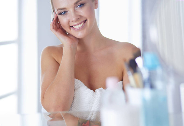 Young woman in bathrobe looking in bathroom mirror - Zdjęcie, obraz