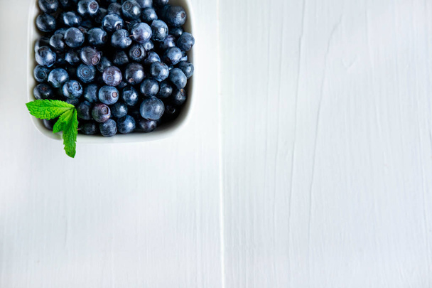 Closeup of blueberry berries with mint leaves in a clay plate on a light wooden background. Photo of blueberry for designers on the banner. Useful berries for sight - Foto, afbeelding