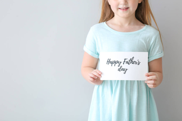 Cute little girl with greeting card for Father's Day on light background - Фото, изображение