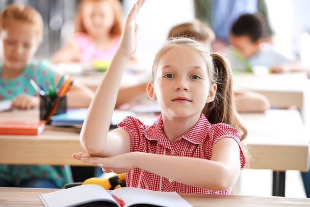 Nettes kleines Mädchen hebt die Hand während des Unterrichts im Klassenzimmer - Foto, Bild