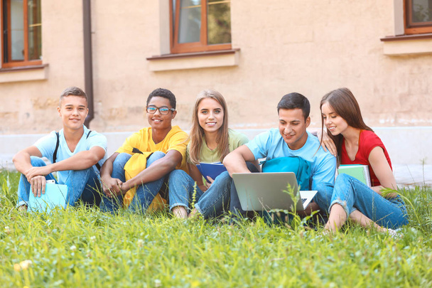 Retrato de jóvenes estudiantes con portátil sentado en la hierba al aire libre
 - Foto, Imagen