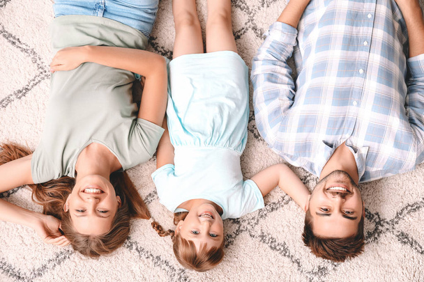 Portrait de jeune famille heureuse allongée sur le tapis à la maison
 - Photo, image