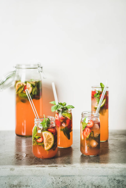 Homemade strawberry and basil lemonade or ice tea in glass tumblers with eco-friendly plastic-free straws on grey concrete table, white wall at background, copy space. Summer refreshing soft drink - Φωτογραφία, εικόνα