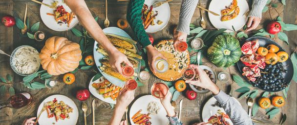 Vegan, vegetarian Thanksgiving, Friendsgiving holiday celebration. Flat-lay of friends clinking glasses at Thanksgiving Day table with pumpkin pie, vegetables, fruit, wine, top view, wide composition - Fotoğraf, Görsel