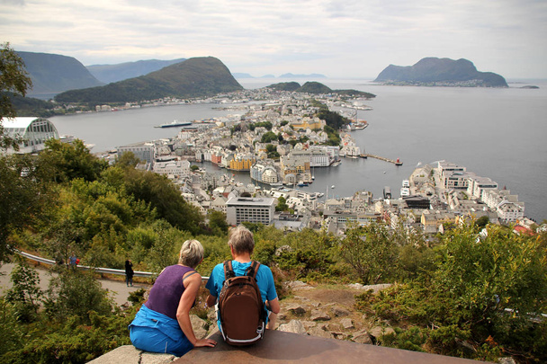 a man and a woman are sitting on the top of Mount Axla, high above the city of Alesun, Norway - Фото, зображення