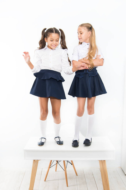Childhood happiness. School day. Kids cute school students stand on table. On same wave. On the top. Popular girls in classroom. School friendship. Schoolgirls tidy appearance school uniform - Photo, image