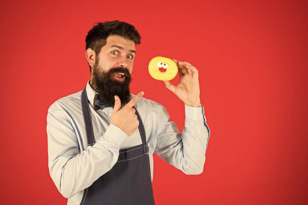 Cheat meal. Hipster bearded baker hold glazed donut on red background. Cafe and bakery concept. Sweet donut from baker. Man bearded baker in cooking apron hold cute dessert. Forget about diet - Photo, image