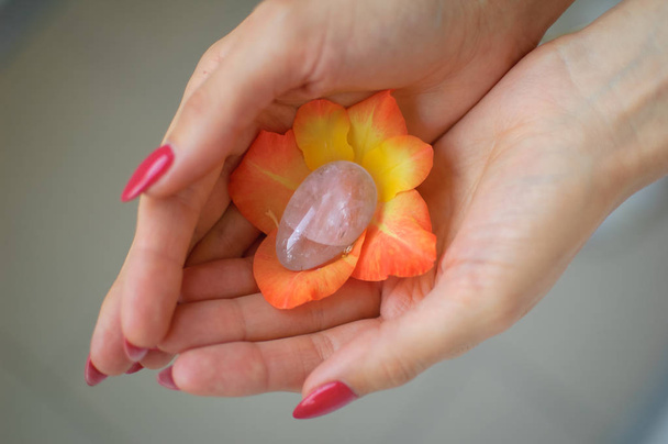 Main féminine avec manucure rouge tenant l'oeuf de yoni améthyste violet transparent pour vumfit, imbuilding ou méditation à l'intérieur fleur de gladiole orange et jaune
. - Photo, image